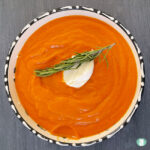 bowl of orange soup with a dollop of cream and sprig of rosemary