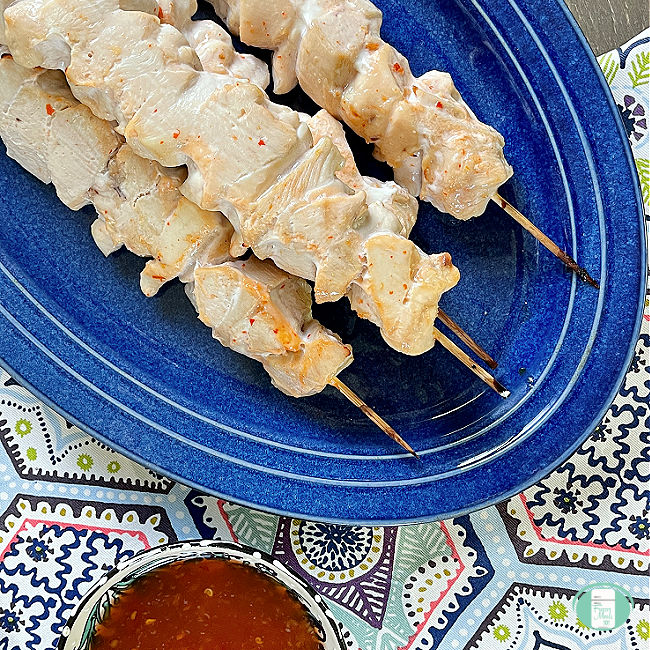 chicken skewers on a blue tray next to dipping sauce