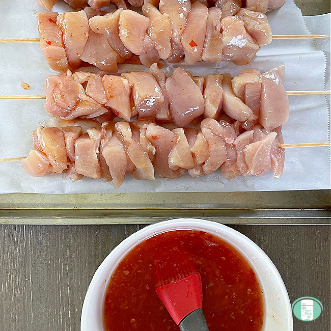 raw chicken chunks on wooden skewers next to a sauce