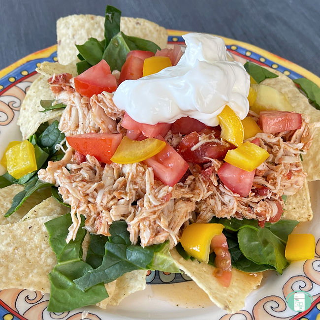 nacho chips topped with shredded chicken, lettuce, tomatoes, and sour cream on a plate