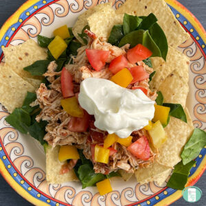 plate of nacho chips with shredded chicken, toppings, and sour cream