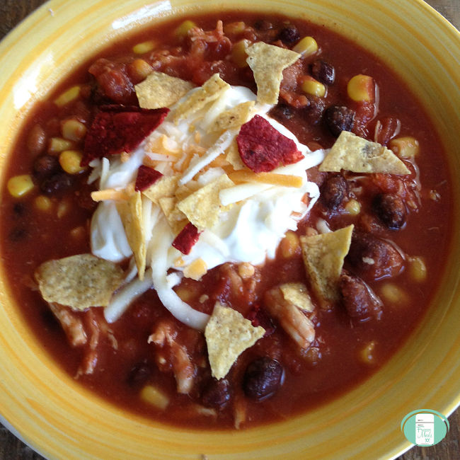 yellow bowl of soup with beans and corn topped with sour cream and crumbled tortilla chips