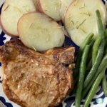 pork chop, green beans, and potato slices on a plate