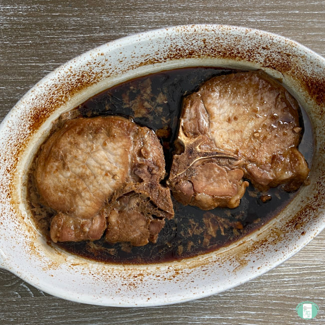 two pork chops in brown sauce in a white baking dish