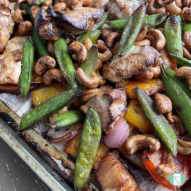 baking sheet with cashews, chicken, and vegetables cooked on it