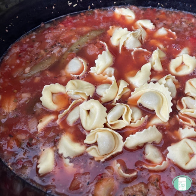 tortellini sits on top of red soup in a slow cooker