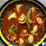 bowl with red soup with tortellini pasta and vegetables in it