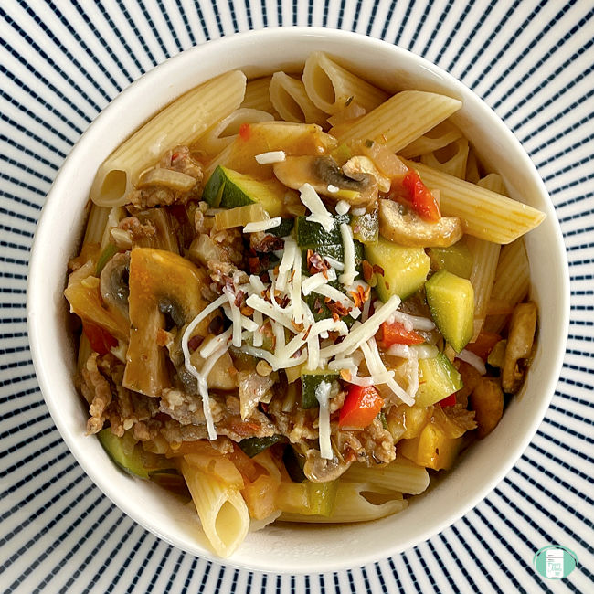 white bowl of pasta topped with sauce with chunky vegetables