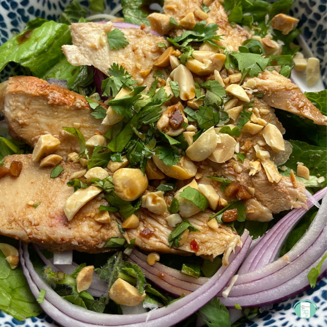 chicken slices topped with peanuts and herbs on top of lettuce