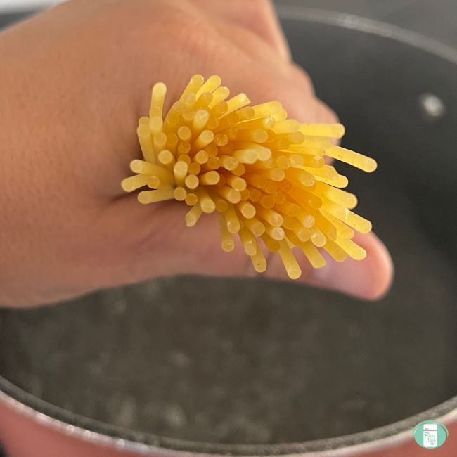 spaghetti noodles held in a fist over a pot of boiling water