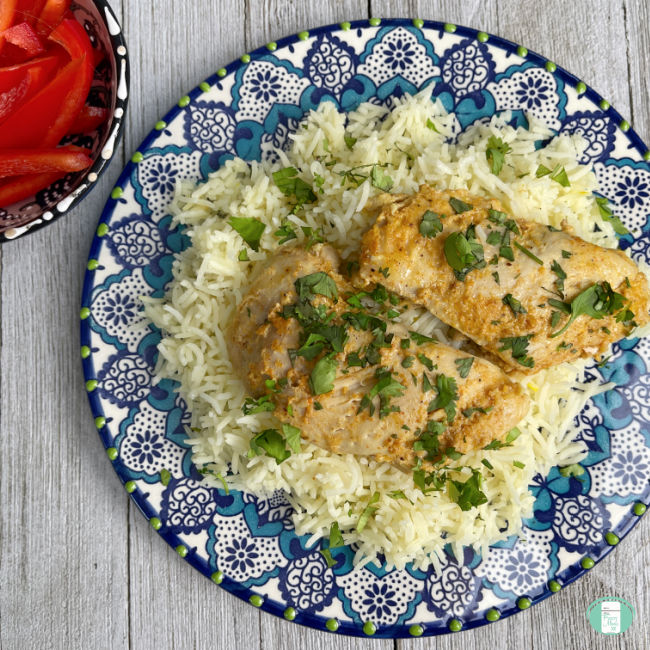 chicken sprinkled with green herbs on top of a bed of rice on a plate