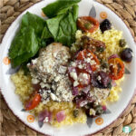 chicken, tomatoes, black olives on couscous next to spinach on a plate