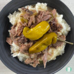 pulled roast beef with pepperoncini peppers on top of mashed potatoes in a bowl