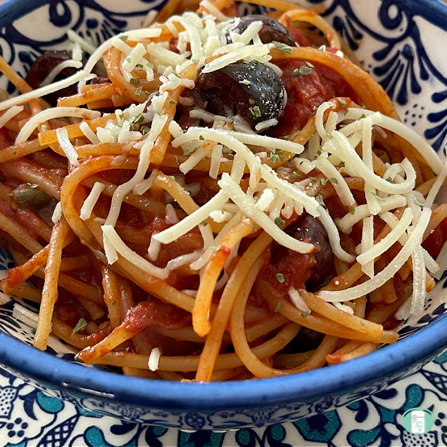 spaghetti noodles in red sauce topped with sprinkled Parmesan cheese and black olives