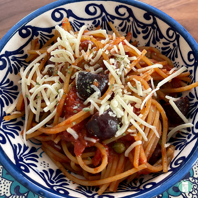 bowl of spaghetti topped with black olives and sprinkled with Parmesan cheese