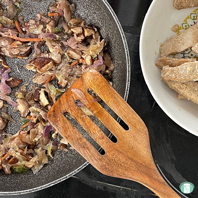 cabbage and mushrooms frying in a fry pan with a wooden spatula