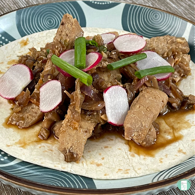 flour tortilla topped with pork slices, sauce, and sliced fresh radishes and green onions