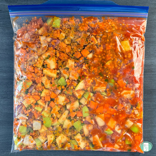 Ingredients for Mulligatawny Soup in a freezer bag. Diced green apples, sliced carrots, onions, lentils, and sauce can be seen.