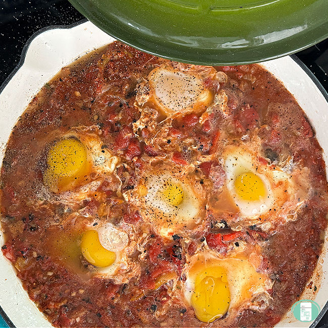 red sauce in a skillet with six eggs poaching in the sauce
