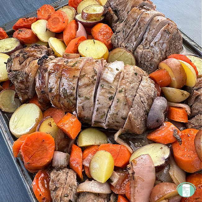 Close up, top down view of a pork tenderloin sliced with baby potatoes and carrots baked and ready to eat. 