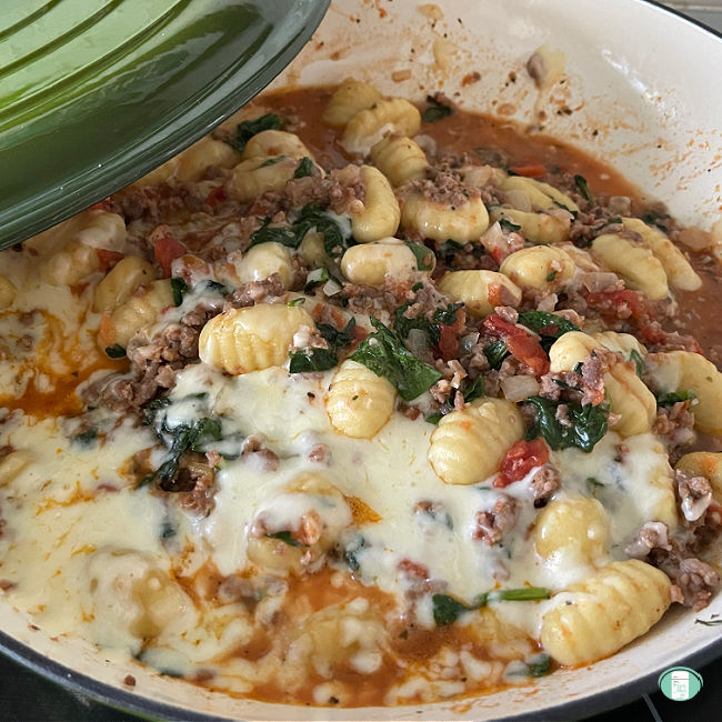 Close up of the skillet as the lid is removed and the cheese is melted on gnocchi, ground sausage, and spinach. 