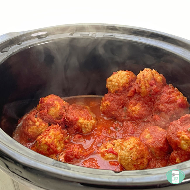 meatballs in red sauce cooking in slow cooker with steam coming off them