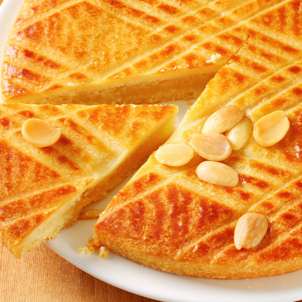 A tight shot of a slap of Boterkoek (Dutch Butter Cake) with a serving cut out and garnished with almonds. 