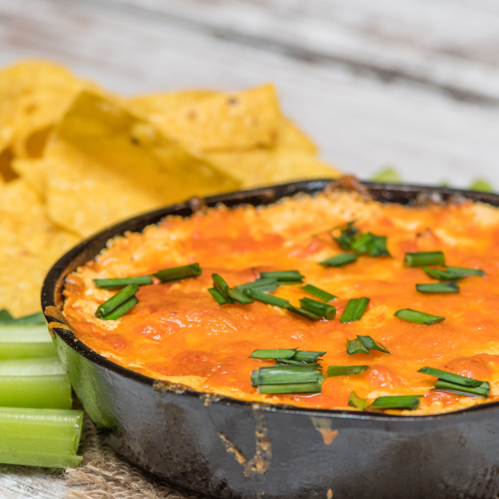 Buffalo Chicken Dip served in a black bowl and topped with chopped green onions, alongside celery sticks and taco chips