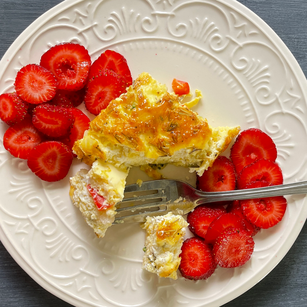 A square of frittata served on a plate with some sliced strawberries
