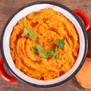 Overhead shot of sweet potato casserole in a red handled casserole dish, garnished with a stem of cilantro