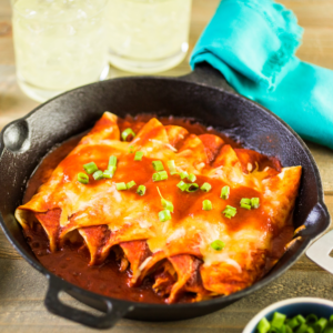 Turkey Enchiladas rolled, side by side in a cast iron pan, smothere in cheese, enchilada sauce and sprinkled with chopped greenonions