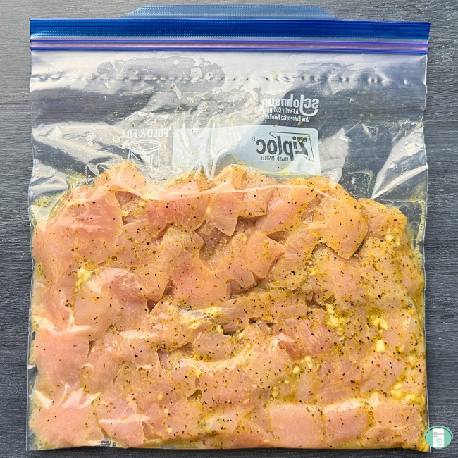 All of the ingredients for Lemon Pepper Chicken Bites in a freezer quality bag: chicken breasts, lemon juice, garlic, lemon pepper, oregano, cayenne, olive oil.