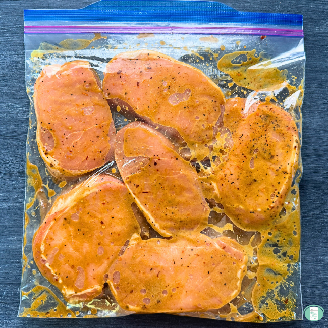 Six pork chops are marinating in a freezer-quality bag.