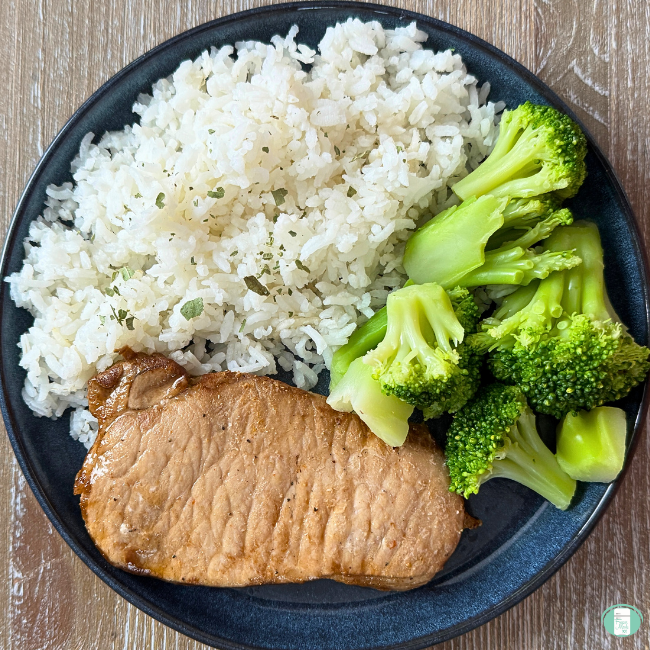 Sweeet and Spicy pork chops with rice and broccoli on a black plate.