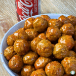 Cola Meatballs in a blue bowl on a brown table. Can of coke in the background.