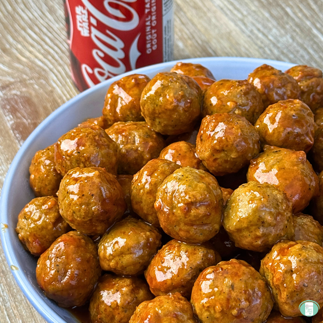 Cola Meatballs in a blue bowl on a brown table. Can of coke in the background.