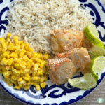 Plate of Smoky Tequila Lime Chicken served with fluffy white rice, sweet yellow corn, and fresh lime wedges on a blue and white patterned dish.