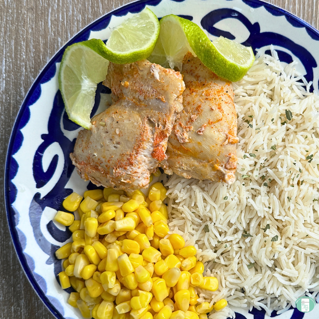 Plate of Smoky Tequila Lime Chicken served with fluffy white rice, sweet yellow corn, and fresh lime wedges on a blue and white patterned dish.