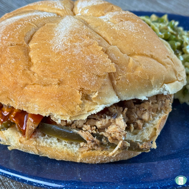 Texas pulled pork sandwich on a soft sandwich roll with tender shredded pork, sliced jalapeños, and barbecue sauce, served on a blue plate with a side of coleslaw.