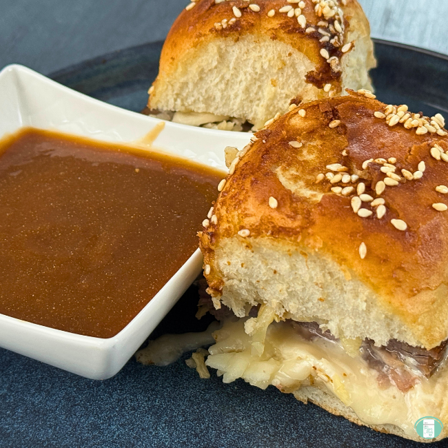two roast beef sliders on a plate next to a small bowl of gravy