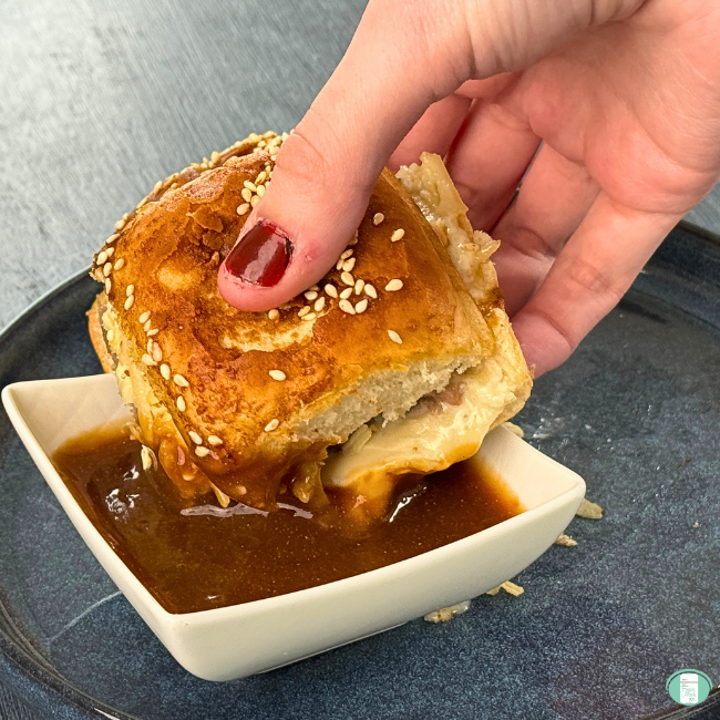 Hand holding beef slider, dipping in gravy.
