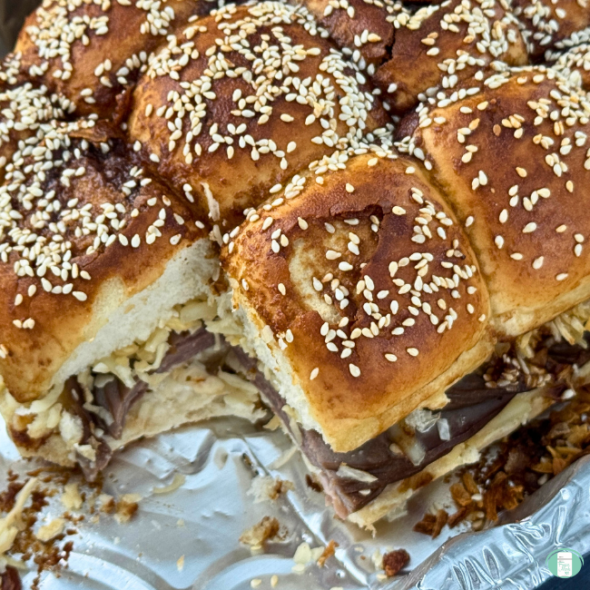 Roast beef sliders on sesame bun in foil tray.