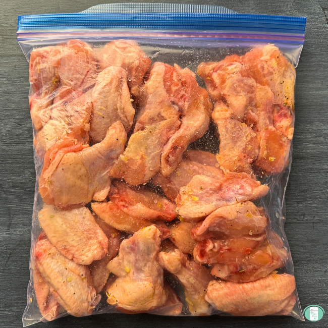 Raw, seasoned chicken drumsticks and wings in plastic freezer bag.