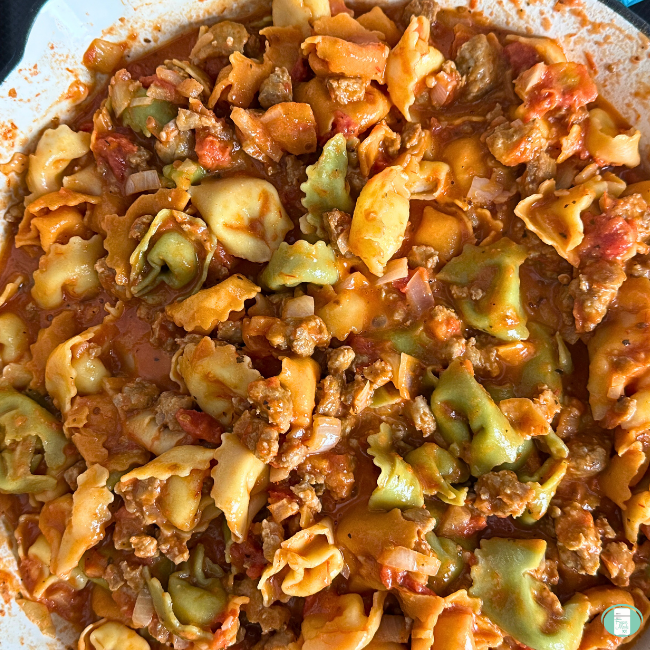 colourful tortellini with sausage, tomatoes in white bowl.