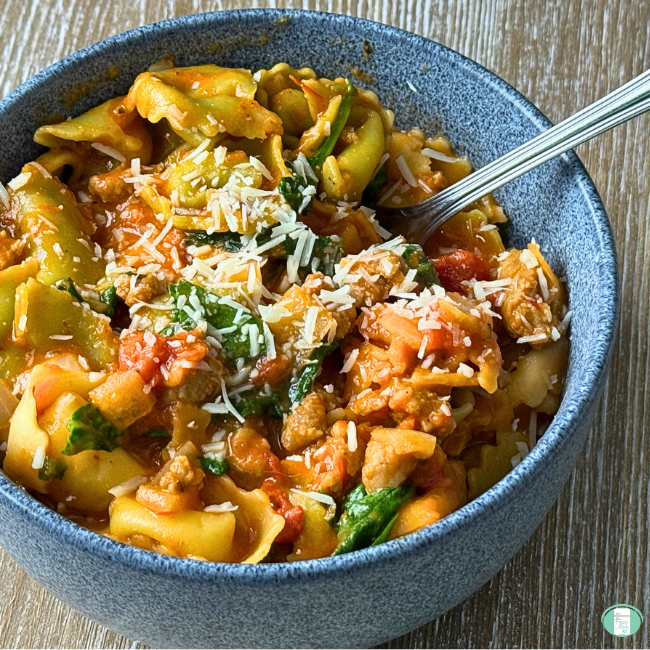 tortellini with sauce, sausage and spinach with parmesan in blue bowl.