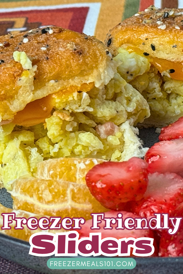 two buns filled with scrambled eggs, bacon, and melted cheese topped with melted butter and sesame seeds next to oranges and strawberries on a plate