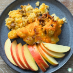 tater tots with eggs, sausages and cheese with apple slices on blue plate