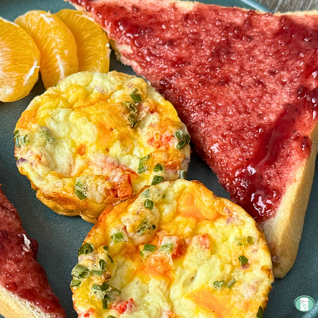 Cooked cottage cheese egg bites with orange slices, bread with jam on green plate.