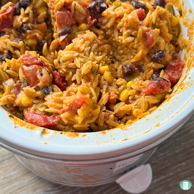 Cooked Enchilada Orzo meal with tomatoes, beans, corn in slow cooker.