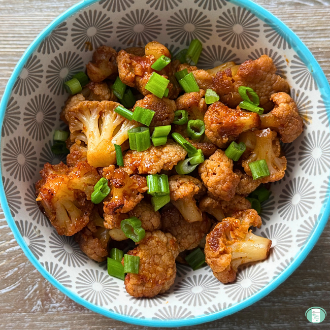 Cauliflower in sauce in bowl sprinkled with green onions.